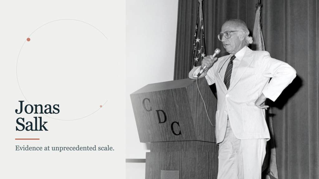 Jonas Salk phát biểu tại bục của CDC ở bên phải trong bố cục biên tập tối giản với một họa tiết hình tròn mờ nhẹ.